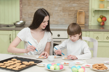Obraz na płótnie Canvas Young mum and her little son baking together and decorating the cupcakes