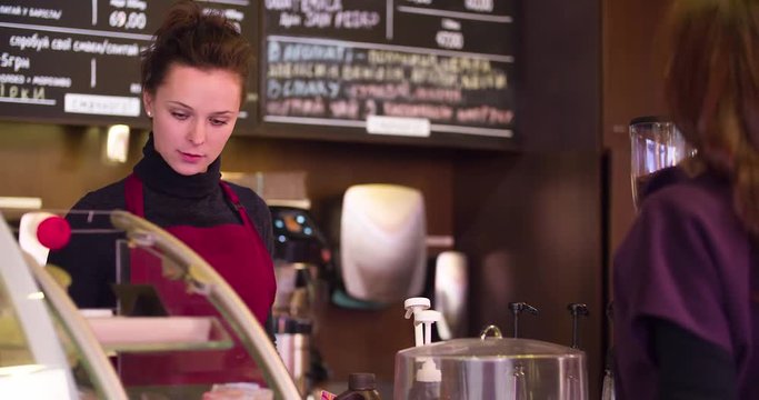 Woman makes an order at cafe bar in coffee shop HD video. Barista interacts with customer