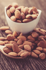 almonds in a white ceramic bowl with wood spoon on grained wood background