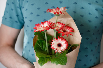 Young man holding flower pot with red gerbera daisies in paper envelope.Concept of holiday and gifts.
