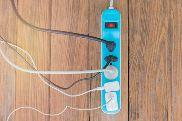 Many electrical cords connected to a single power strip or extension block. on a wooden floor