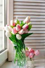 Beautiful mottled tulips bunch in glass vase at window with spring nature. Parrot tulips bouquet