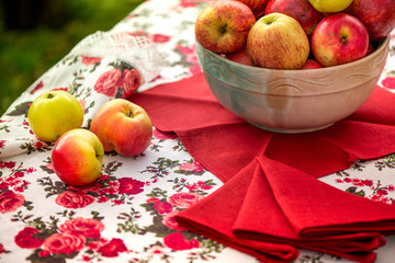 Golden autumn. Macro shot of natural linen tablecloth with rose print and crochet white lace trim, red linen napkins and a bowl, full of red and yellow apples on top of the table on green background