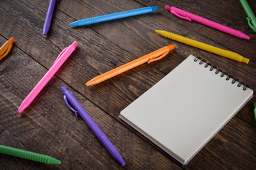 colored pens with a notebook on a wooden background place for text