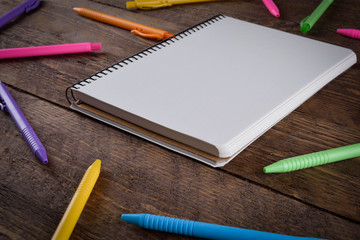 colored pens with a notebook on a wooden background place for text
