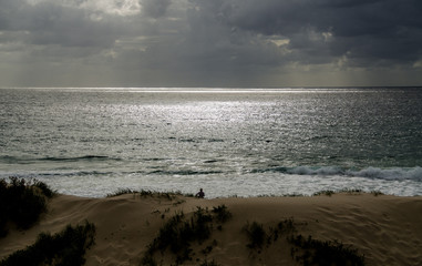 Storm brewing at sea as person sits on remote beach