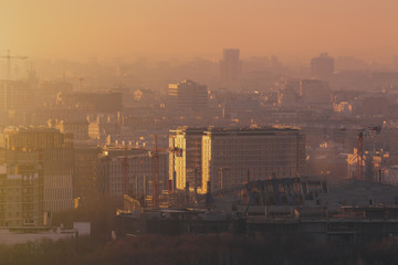 Close-up shooting from top of morning metropolitan city: huge stadium under construction with cranes and beams, residential buildings and districts, multiple facades, hazy horizon, Moscow, Russia