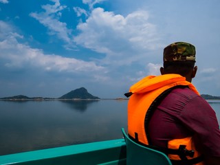 Man wearing orange color life jacket traveling in a boat taking a boat ride tour in a lake river in a national park in sri lanka