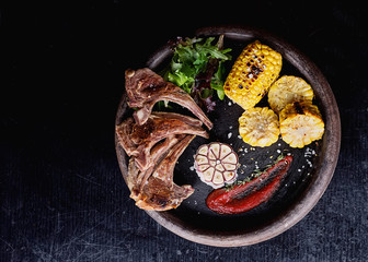 Grilled lamb ribs served with grilled corn, salat, bbq sauce, garlic, salt pepper on a rustic ceramic plate. Top View