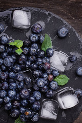 Blueberries on a stone slate board wth ice cubes and mint leaves over a rustic wooden board