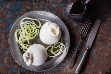  Traditional Italian speciaty Burrata Cheese on a metal rustic plate served with olive oil  and cucumber spaghetti over a rustic wooden board. Dark Rustic style