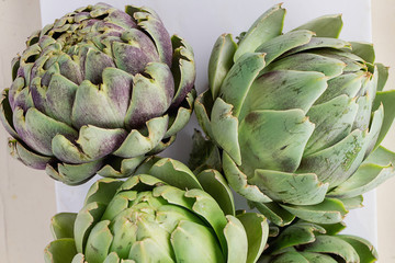 Fresh organic artichokes on a white marble board  over a rustic wooden background. Top View