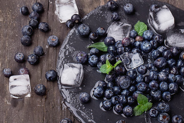 Blueberries on a stone slate board wth ice cubes and mint leaves over a rustic wooden board