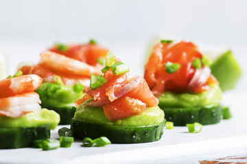 Appetizer with cucumber, avocado, salty trout and shrimp on a white background, selective focus