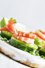 Appetizer with cucumber, avocado, salty trout and shrimp on a white background, selective focus