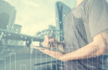 Double exposure of businessman using digital tablet with city landscape blurred background.Forex graph on the business city centre. A metaphor of international financial consulting.investment concept