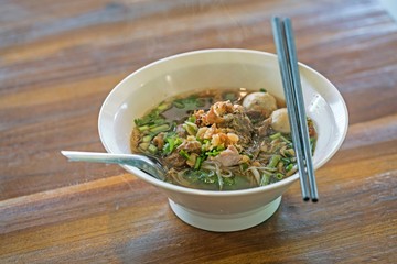 Thai food : Rice noodle soup with stewed pork and pork balls with soup on wooden table.
Thai Noodles style.