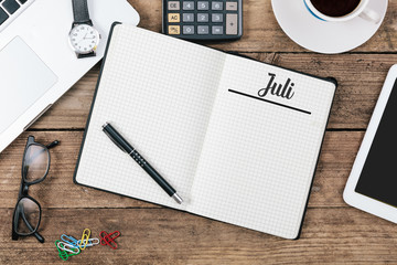 Juli (German July) month name on paper note pad at office desk