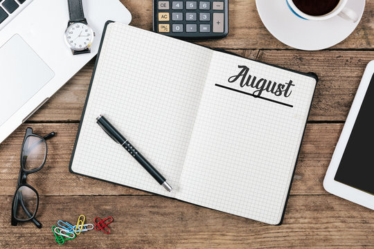 August (German and English) month name on paper note pad at office desk