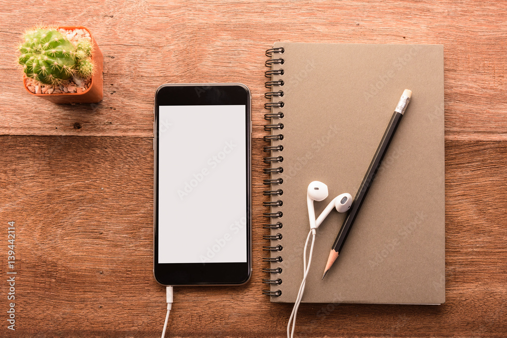 Poster smartphone with white screen and note book on wooden table with copyspace
