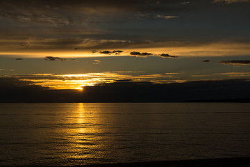 Beautiful golden sunset at calm adriatic sea, last beam of the sun makes a golden path on waveless water surface. Enlighted with orange light clouds on background.