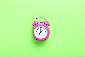 Pink alarm clock on the green background