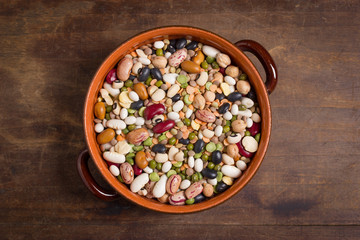 Mix of colorful beans and lentils in rustic bowl on wooden background. Top view.