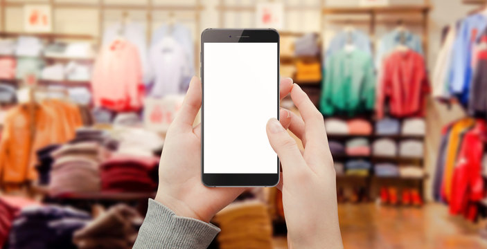 Women in clothing store holding black phone in hands and touching screen. Shopping online concept. Mockup of modern black phone, empty screen for text, icons, adverts and other