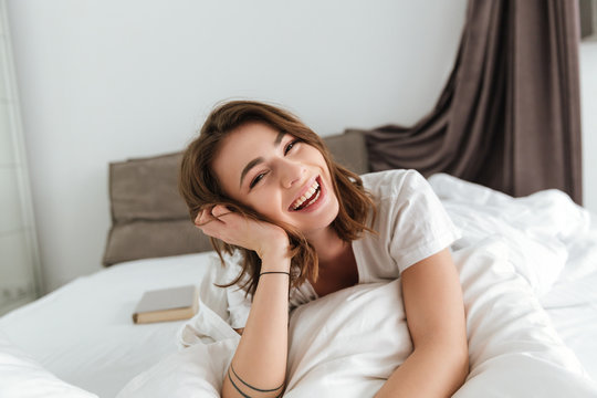 Cheerful cute young woman lying and laughing in bed
