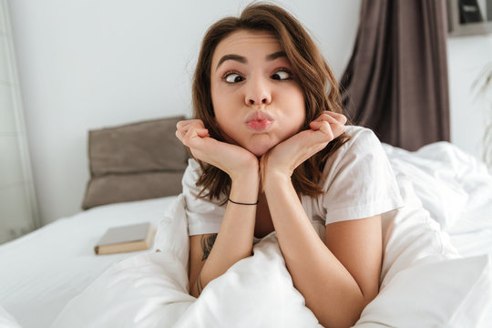 Amusing comical young woman making funny face lying in bed