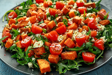 Sweet potato, carrots, cherry tomatoes and wild rocket salad with feta cheese served in black plate
