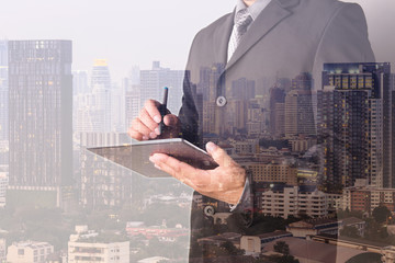 Fototapeta na wymiar Double exposure of Business man working with a digital tablet with cityscape blurred building background, Business Trading concept