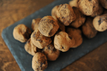 Chocolate truffles in cocoa sprinkled. On the slate board on wooden background. Close-up, texture