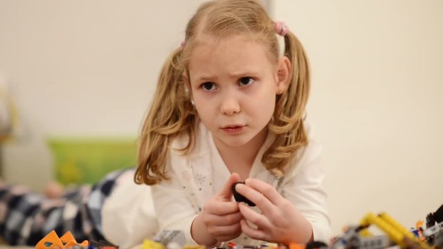 Adorable child girl with funny pigtails playing with constructor on floor
