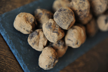 Chocolate truffles in cocoa sprinkled. On the slate board on wooden background. Close-up, texture