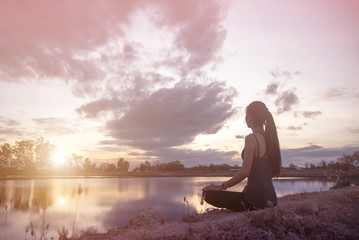 Silhouette of a young woman relaxing on a beautiful sunset. Woman enjoying nature sunset. Serious sad woman. Silhouette of the woman standing lonely at the field during beautiful sunset. Retro image.