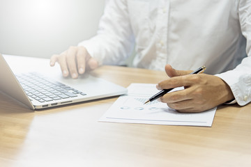 Close up of people working with graph and laptop on his wooden table in the office on business concept