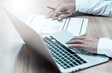 Close up of people working with graph and laptop on his wooden table in the office on business concept