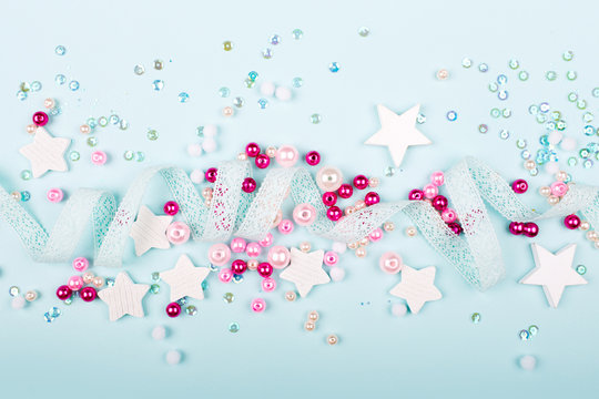 Stylish Frame border with cute decoration:  lace ribbon, stars, sequins and pink pearl beads  with copy space for text on blue background. Flat lay, top view