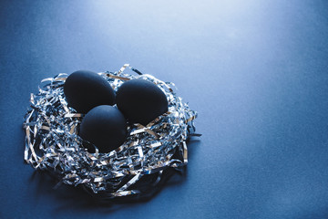 Obraz na płótnie Canvas Three black eggs in a nest made of silver strings, on a dark blue background, Easter concept 