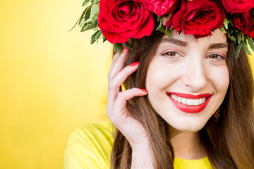 Close-up portrait of a beautiful woman with wreath made of red roses on the yellow background