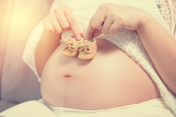 Pregnant woman holding small baby shoes relaxing at home