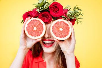Colorful portrait of a beautiful woman with flower wreath holding slices of grapefruits on the...
