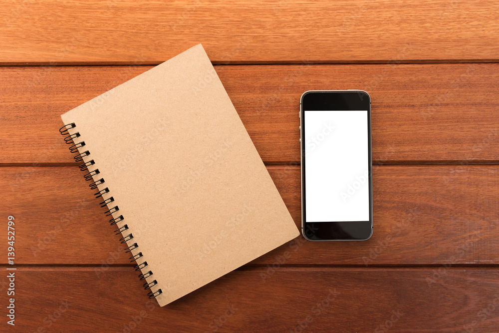 Aufkleber smartphone with white screen and note book on wooden table with copyspace