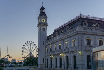 Night sunset view Port Authority buildings with clock tower in Valencia harbor, Spain. Background ferris wheel and moon