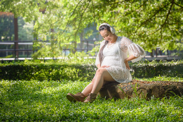 happy pregnant woman listening to a music at park.