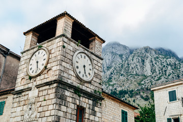Fototapeta na wymiar Clock tower under misty mountains in historical old town of Kotor, Montenegro