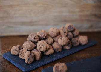 Chocolate truffles in cocoa sprinkled. On the slate board on wooden background. Free space for design