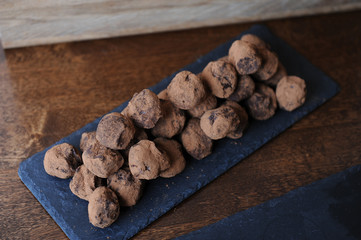 Chocolate truffles in cocoa sprinkled. On the slate board on wooden background. Free space for design