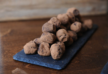 Chocolate truffles in cocoa sprinkled. On the slate board on wooden background. Free space for design